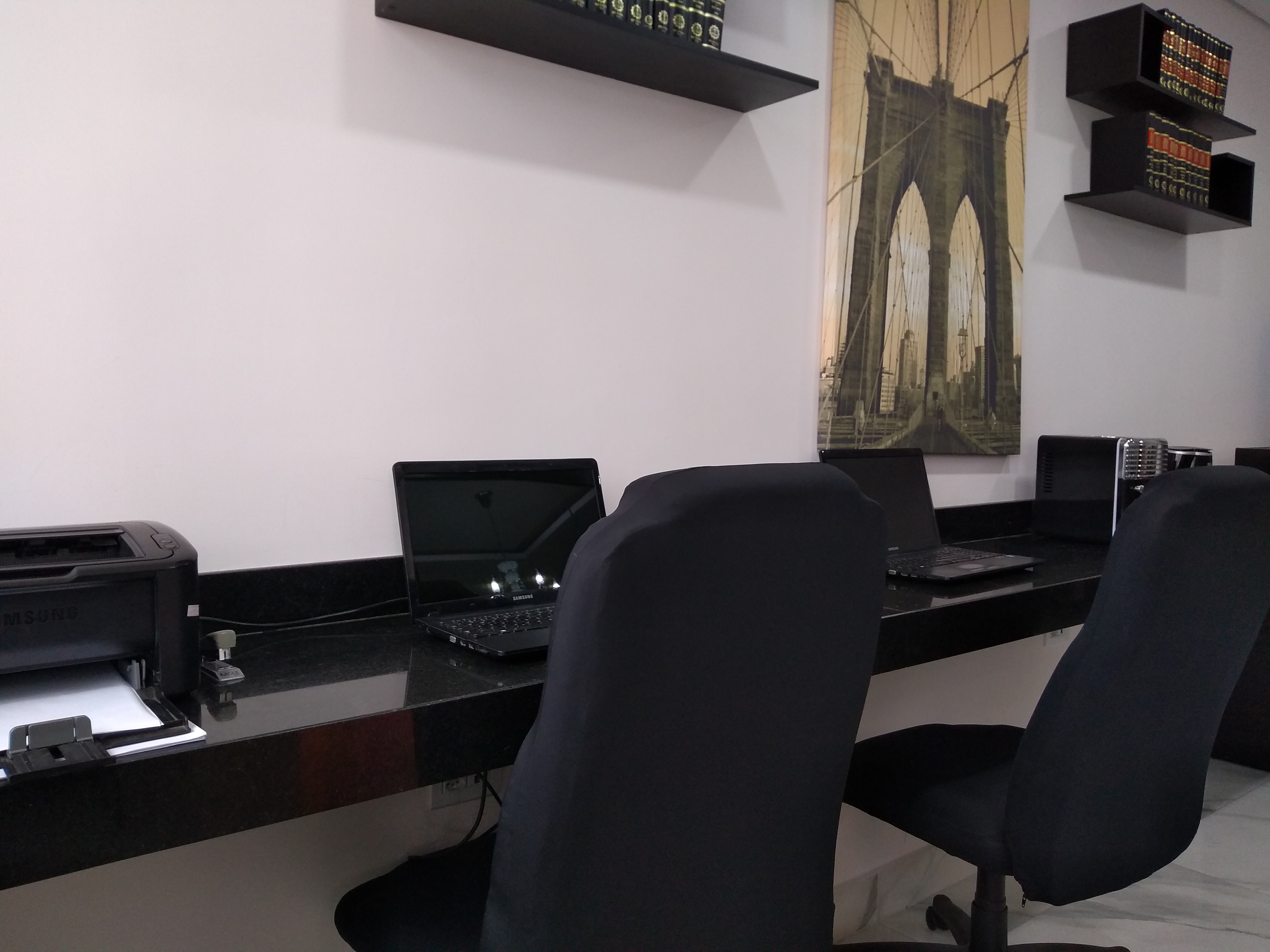 Área de trabalho do escritório, com bancada, computadores e livros jurídicos